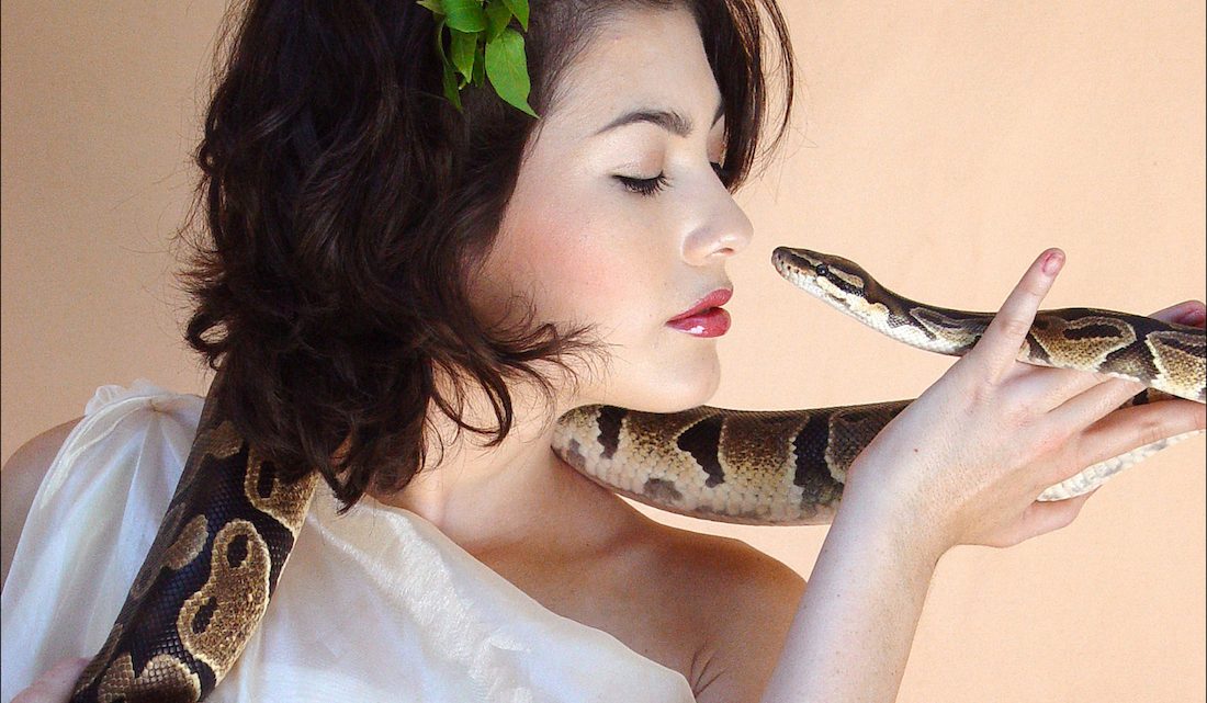Woman (dressed as the Biblical Eve) looking into a snake's eyes
